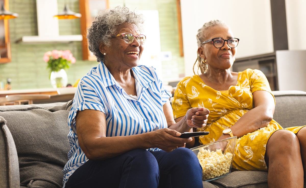 Two older African American women smiling while watching TV.