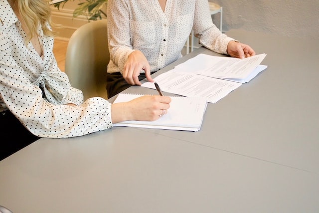 two women sitting at desk with papers on table