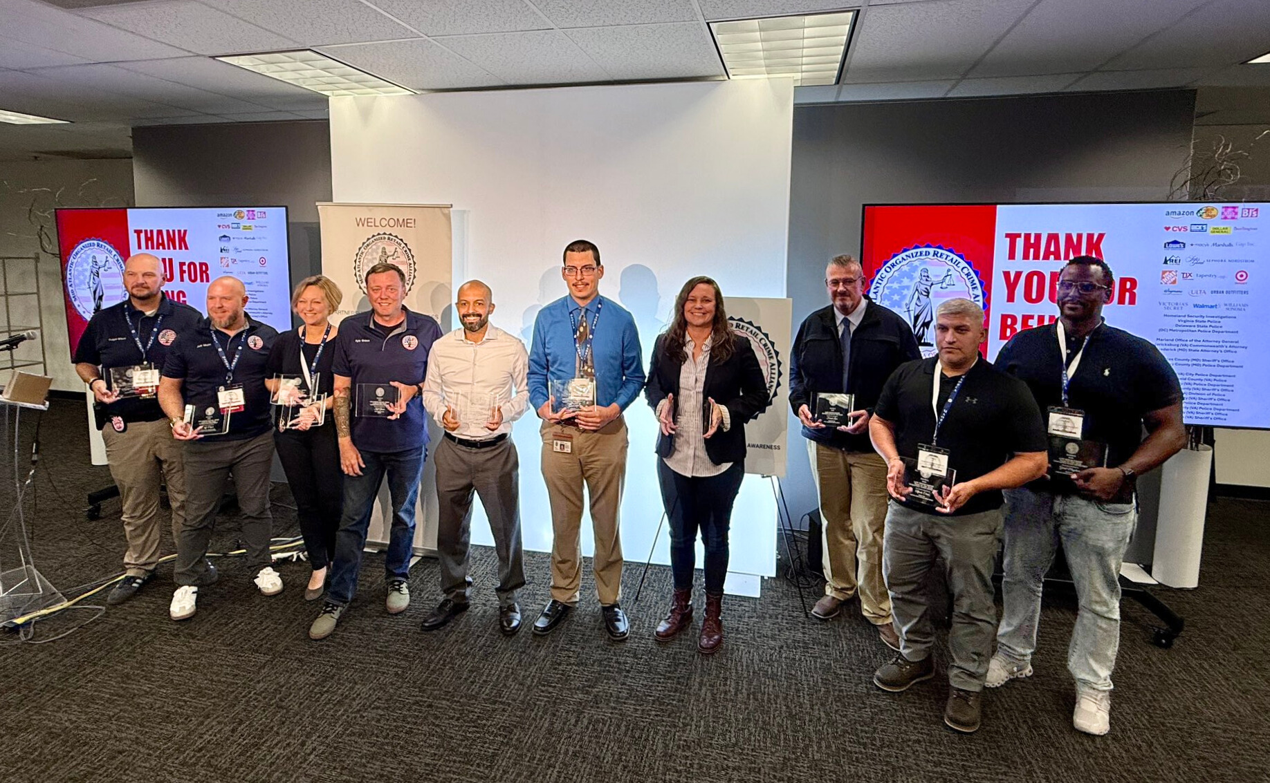 Ten individuals posing with glass awards in front of television screens