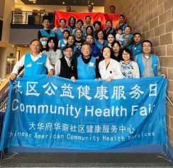 members of the Chinese American Community Health Services pose for a group photo on stairs, holding a blue banner