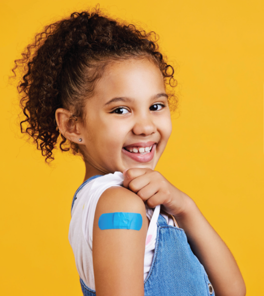 A young girl smiling and showing off a bandage on her upper arm after getting an immunization.