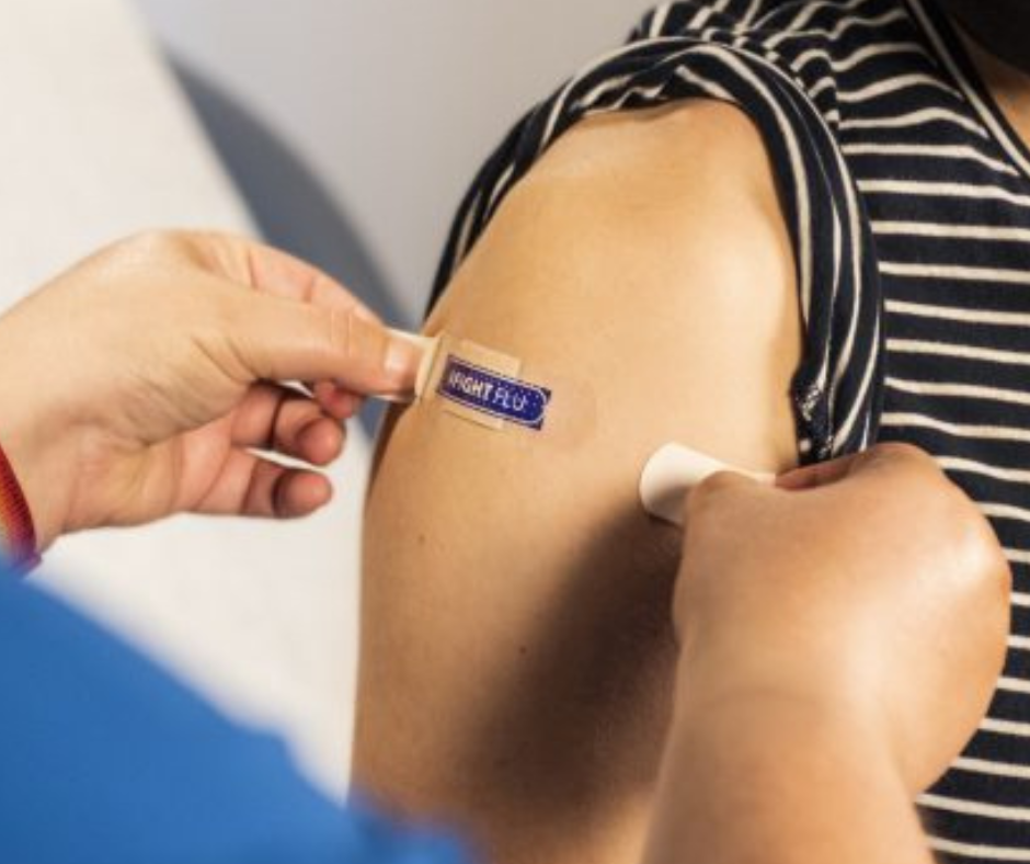 A healthcare provider applies a bandage that says #FightFlu to someone's upper arm.