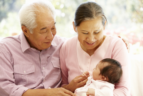 Two smiling grandparents hold a young grandchild