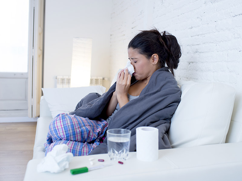 Woman sitting on sofa sneezing into a tissue