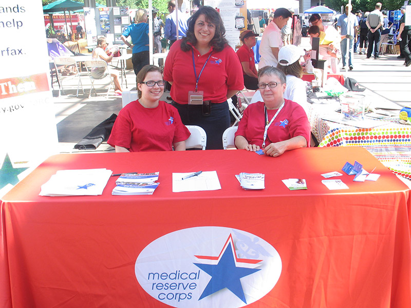 Three Medical Reserve Corps volunteers staff an MRC table at an event