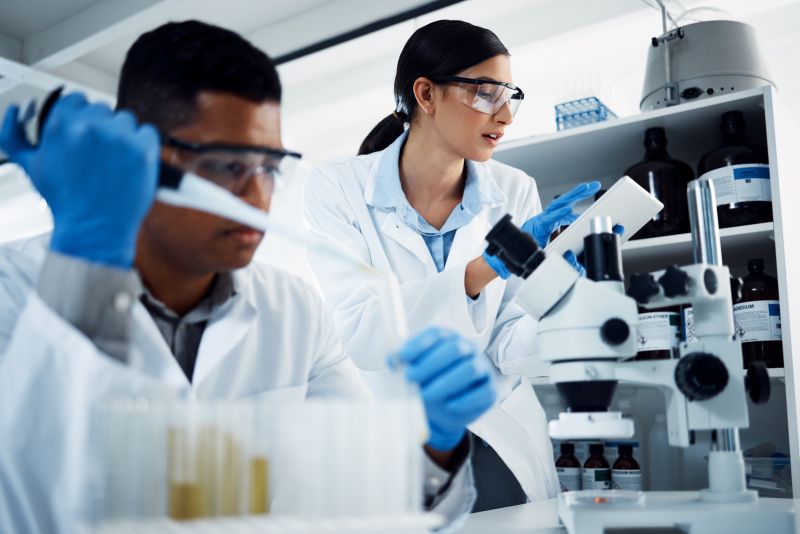 two medical laboratory workers at work, wearing lab coats and goggles