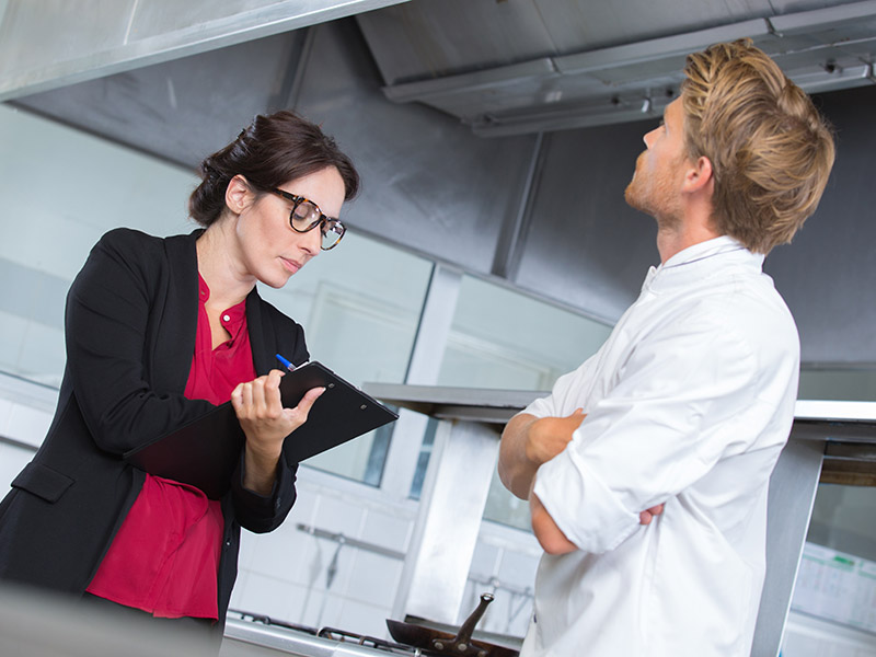 Female inspector takes notes during a restaurant kitchen inspection