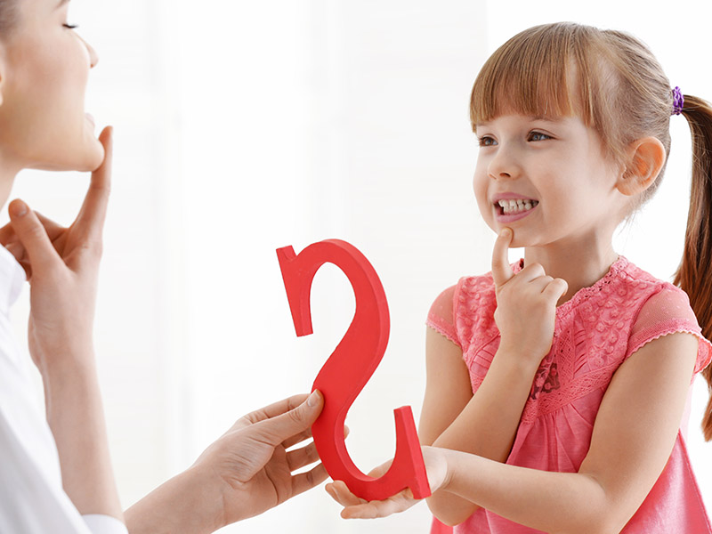 Young girl sounds out the letter S with a female speech therapist