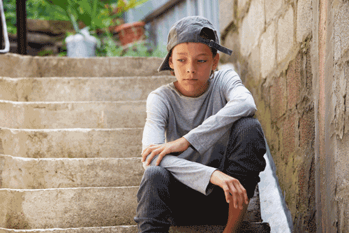 Photo of preteen boy sitting outside on concrete stairs with sad face
