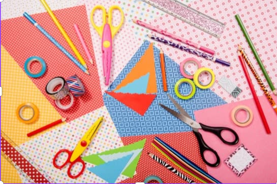 Colorful craft supplies, including patterned paper, scissors, tape and pencils, spread out on a table.