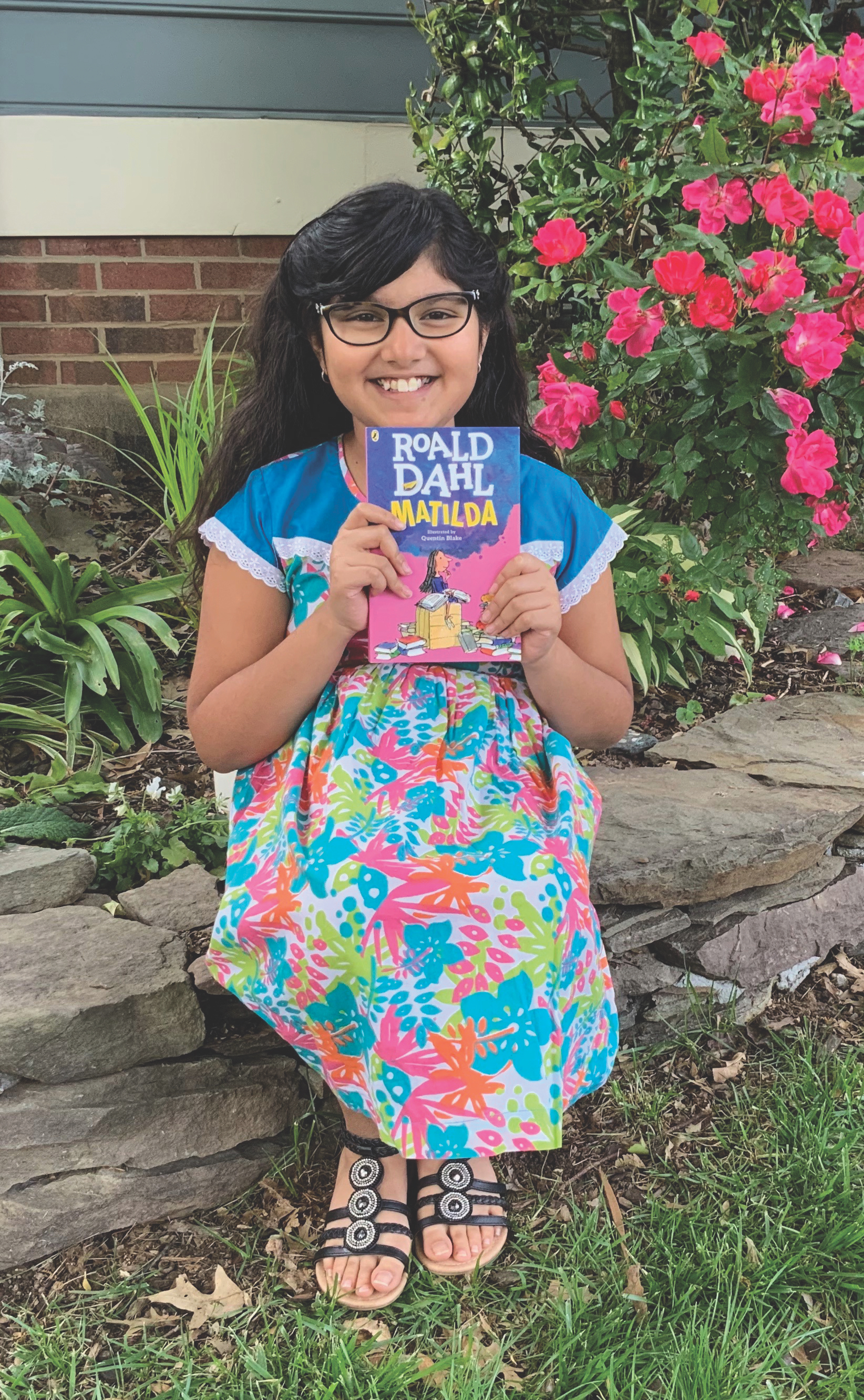 11-year-old girl sits in a garden and holds up the book Matilda by Roald Dahl