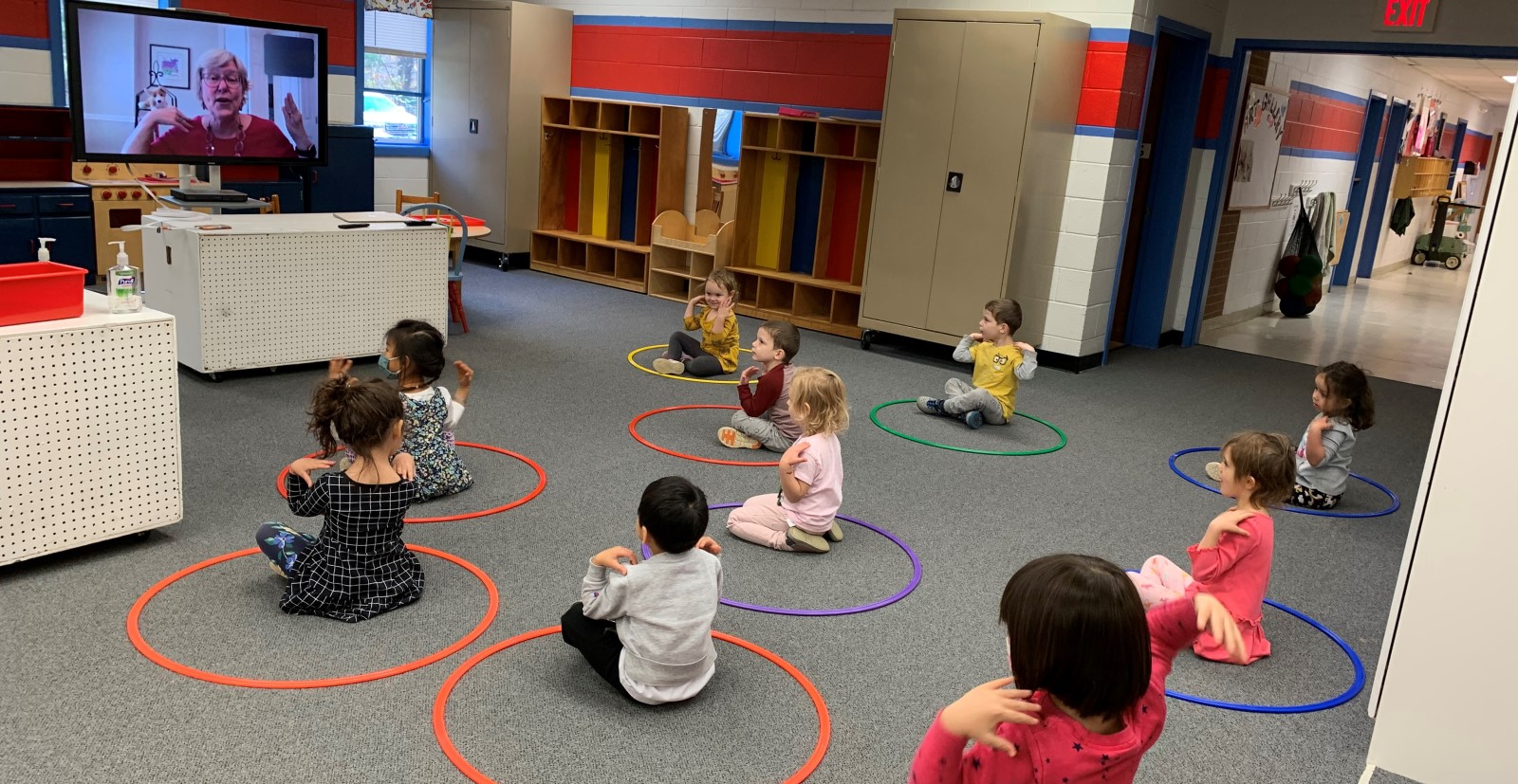 kids in a preschool classroom sit in hula hoops and engage with a live virtual storytime