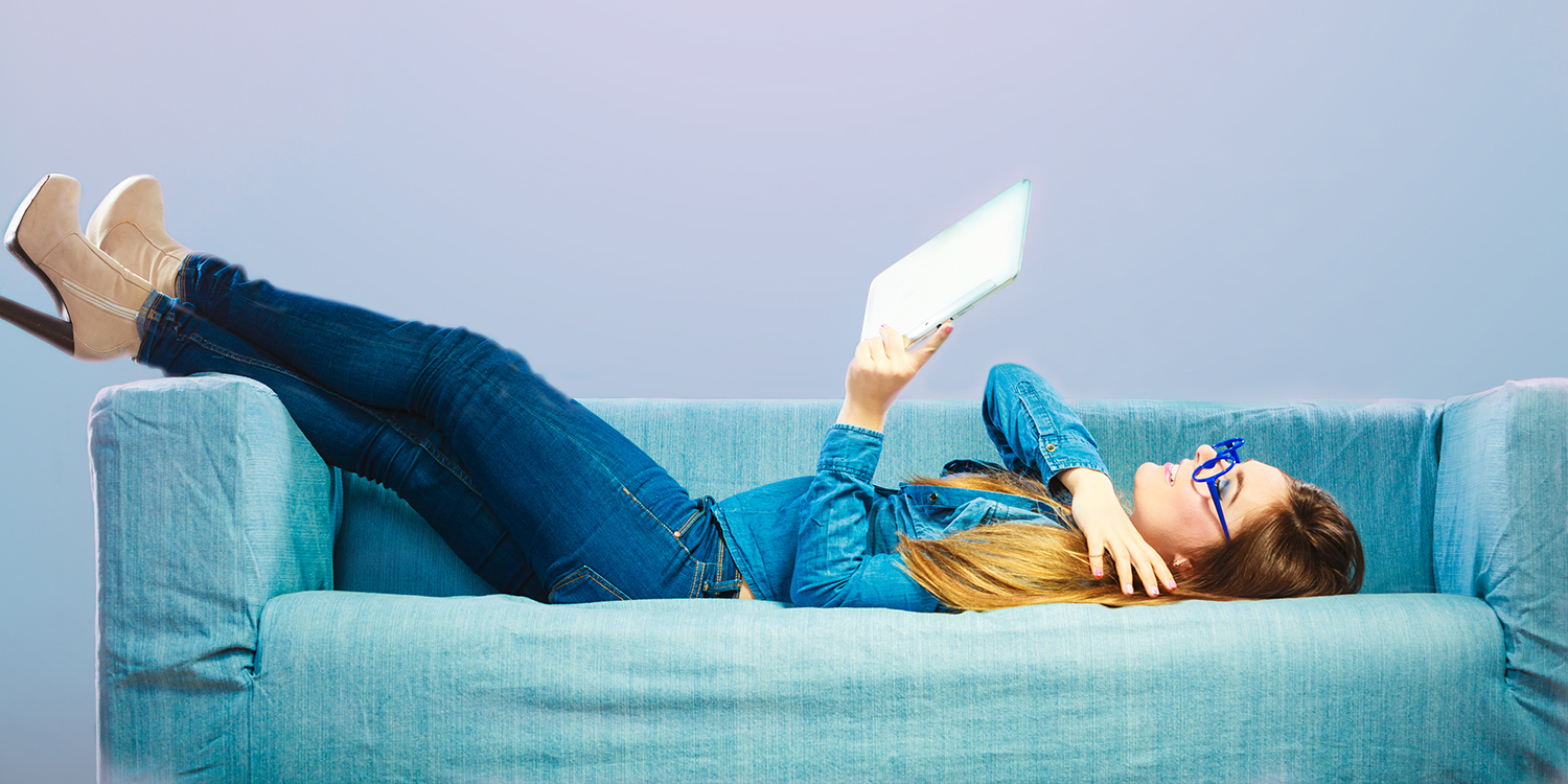 woman laying on couch reading from a tablet
