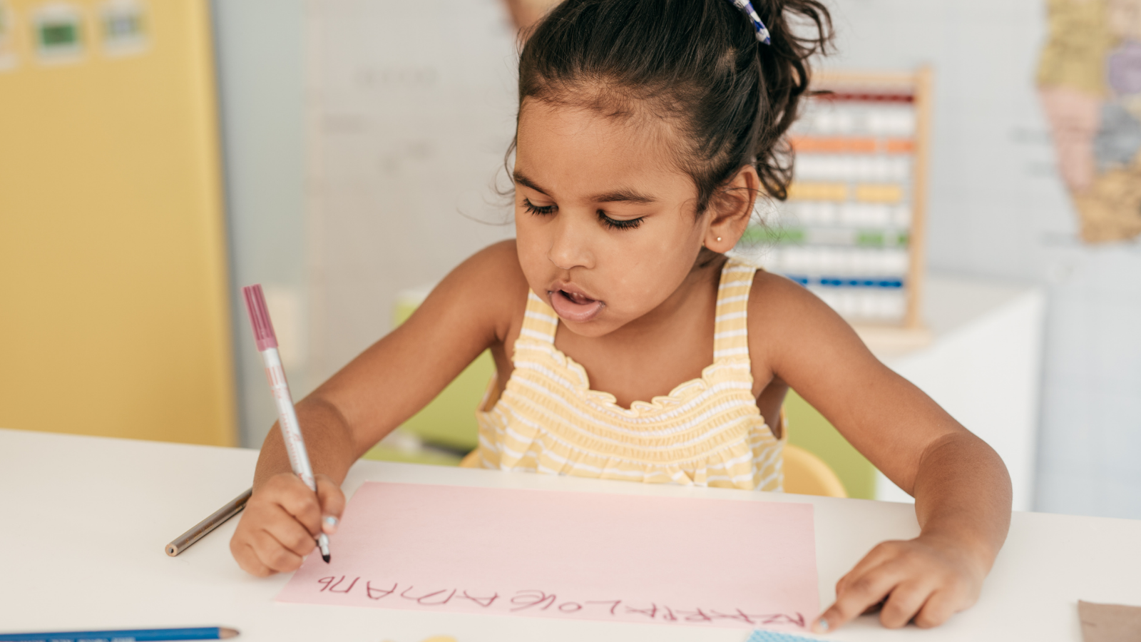 toddler in high chair writes symbols and letters on a piece of paper