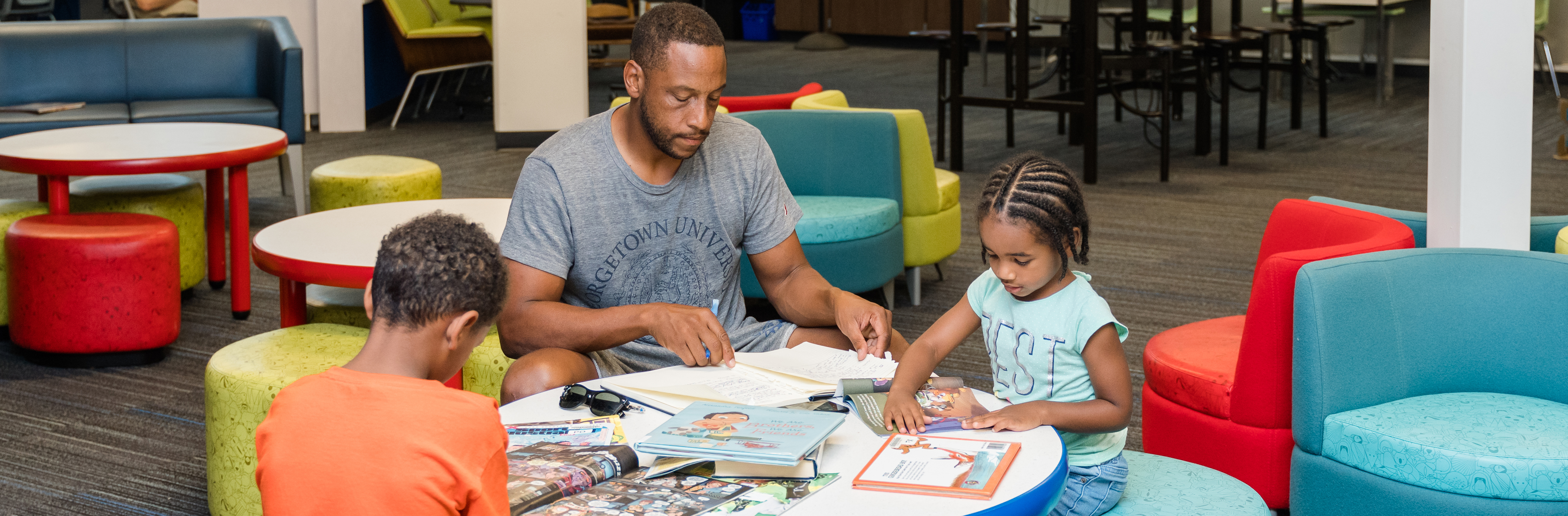 Father and children reading books at table in library