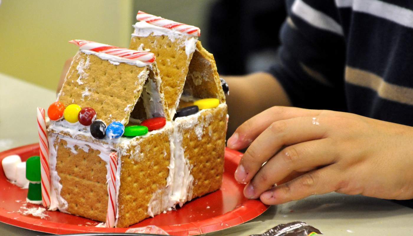 Photo of boy's hands decorating a gingerbread house with M&Ms and frosting