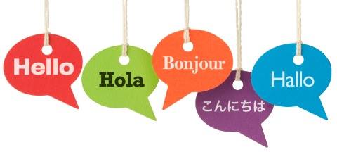 five paper cutout speech bubbles hang from strings and show five translations of "hello": Hello, Hola, Bonjour, Konnichiwa (in Japanese kanji), Hallo