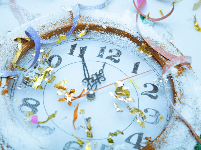 analog clock face approaches midnight with confetti streamers