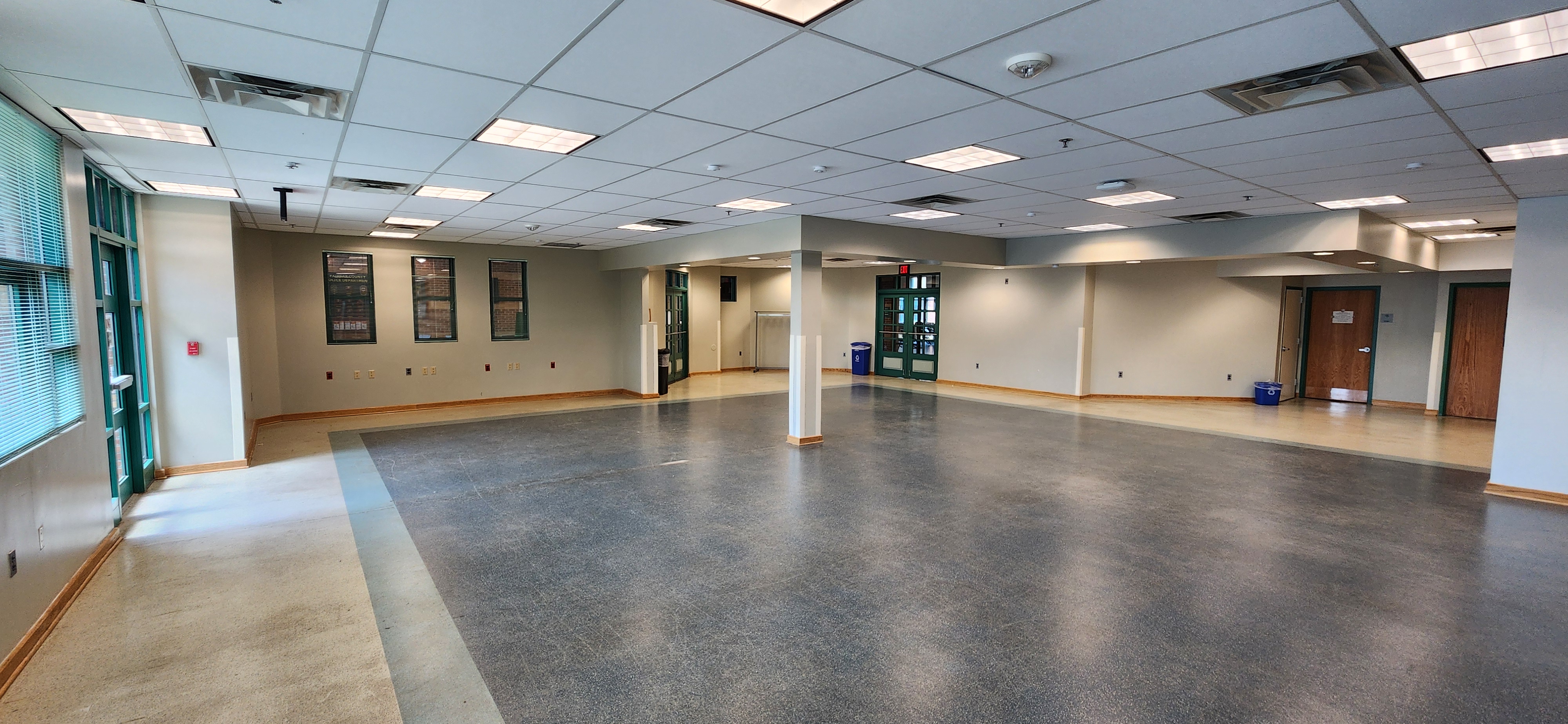 Large open room with tiled ceiling, green-framed windows and doors, support columns, wall vents, and open floor space along neutral walls.