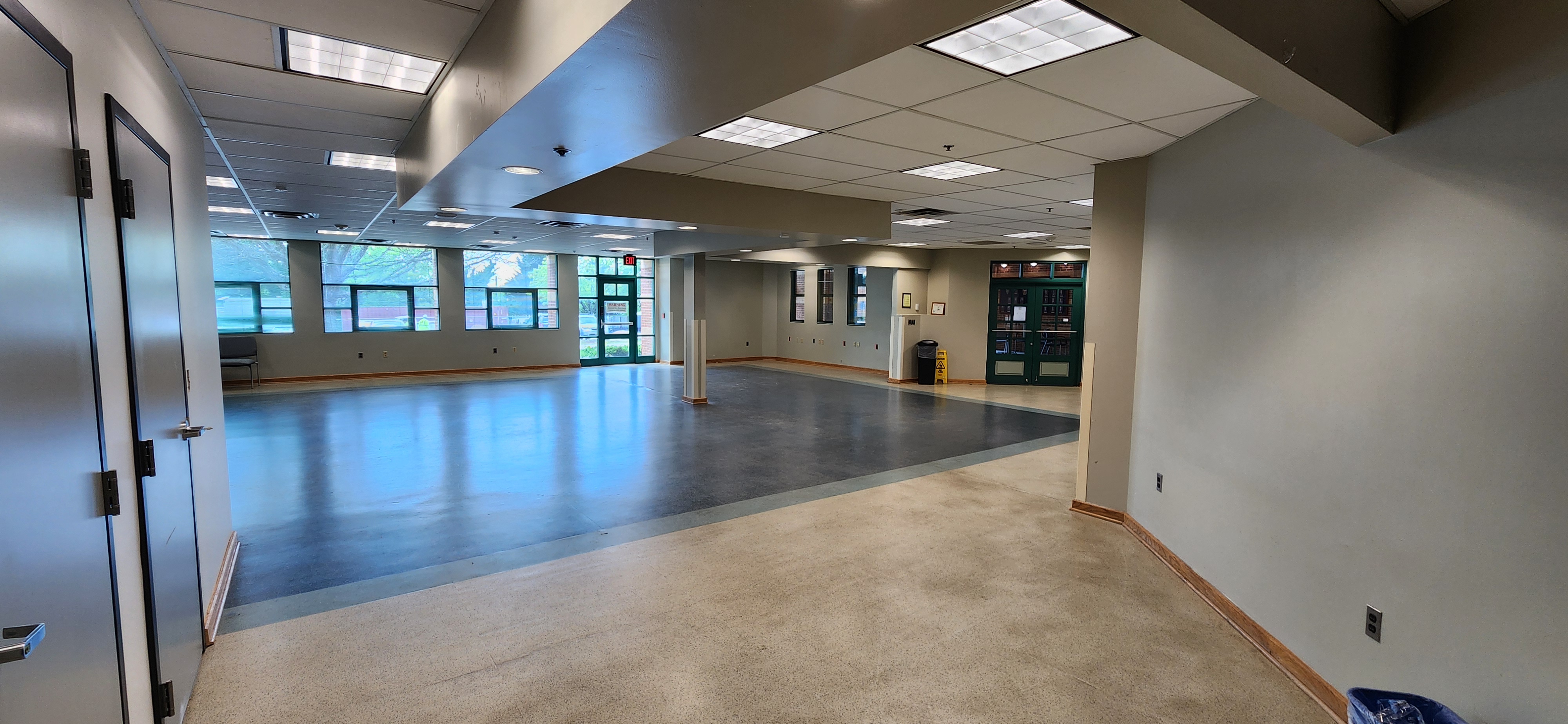 Spacious multipurpose room with large windows, open floor space, support columns, and green doors suited for events, meetings, or classes.
