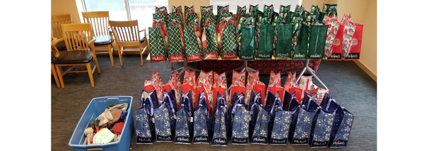 Photo of 35 gift bags lined up on a table and the floor ready to fill with items.