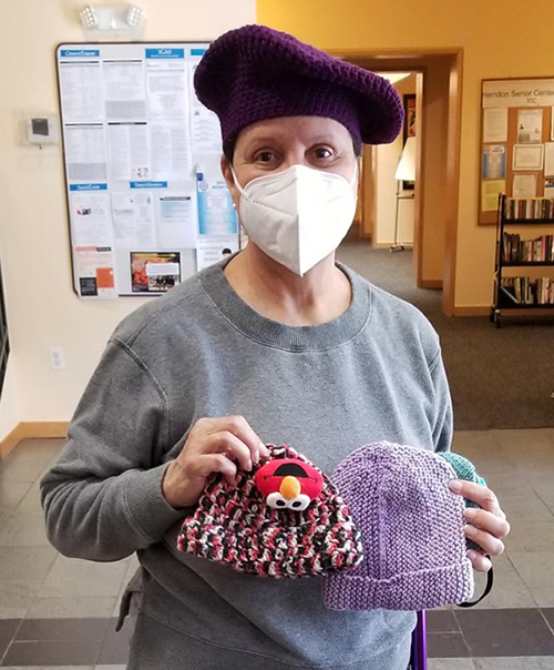 Woman holding knit hats she was donating to the winter warming service project.