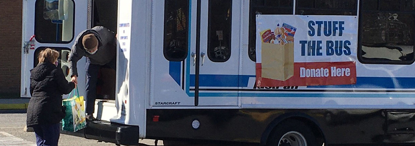 Photo of a woman donating a bag of food to Stuff the Bus at Patrick Henry Library. 