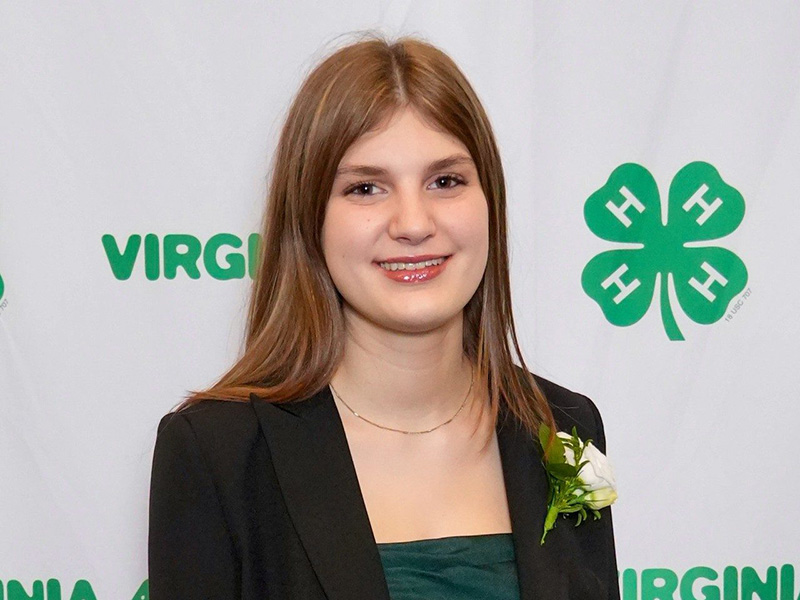 A young woman in professional attire in front of a Virginia 4-H step and repeat banner.