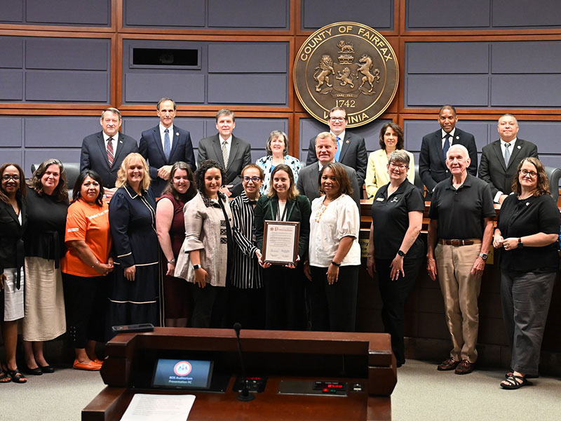 A group of adults smiling and posing with a framed certificate.