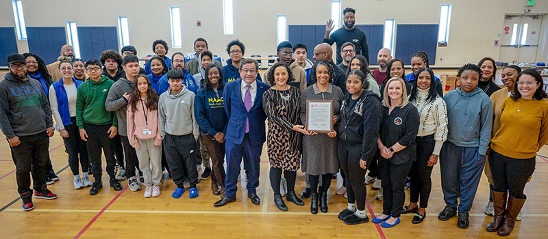 A group of high school students and several adults smiling and posing with a framed certificate.