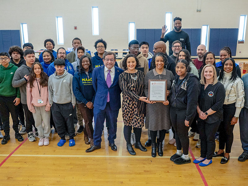 A group of high school students and several adults smiling and posing with a framed certificate.