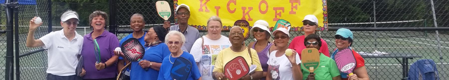 group of older adults smiling at a pickleball court