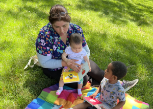 Instructor on blanket outside reading to kids