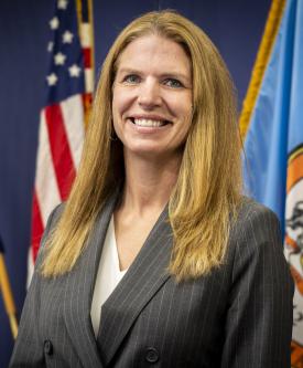 An image of Jen Miller in front of the U.S. and Fairfax County flags.
