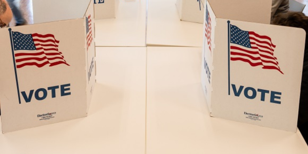 Voting booths with "VOTE" and an American flag printed on them are set up on a table in a polling location.