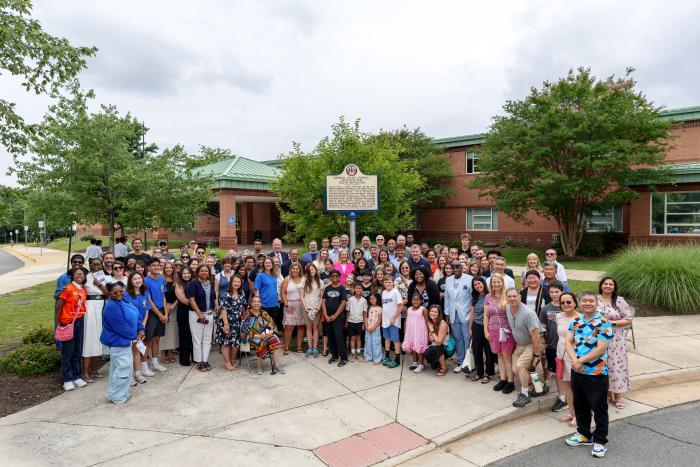 A large group of people consisting of students, educators, community members, board members, and friends and family standing in front of the General Colin L. Powell historical marker.