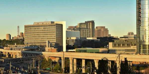 Skyline view of Tysons with several modern mid‑ and high‑rise office buildings, a Metro station, and an elevated rail line in the foreground, all under a clear sky.