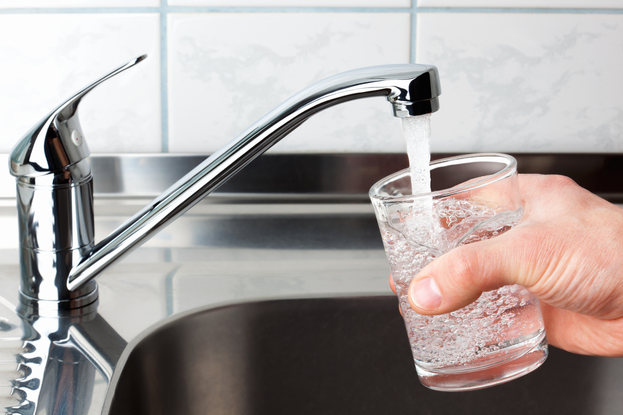 hand holding glass of water as it is filled from kitchen sink tap