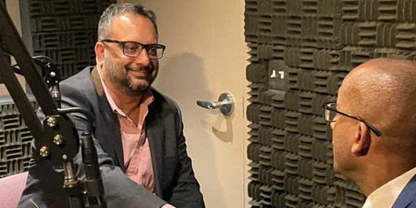 Image of Fairfax County Executive Bryan Hill connects with President and CEO of the Wolf Trap Foundation Arvind Manocha sitting in front of microphones.