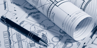 Rolled architectural blueprints resting on top of a detailed site plan, with a black pen placed across the drawings.
