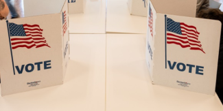 Voting booths with "VOTE" and an American flag printed on them are set up on a table in a polling location.