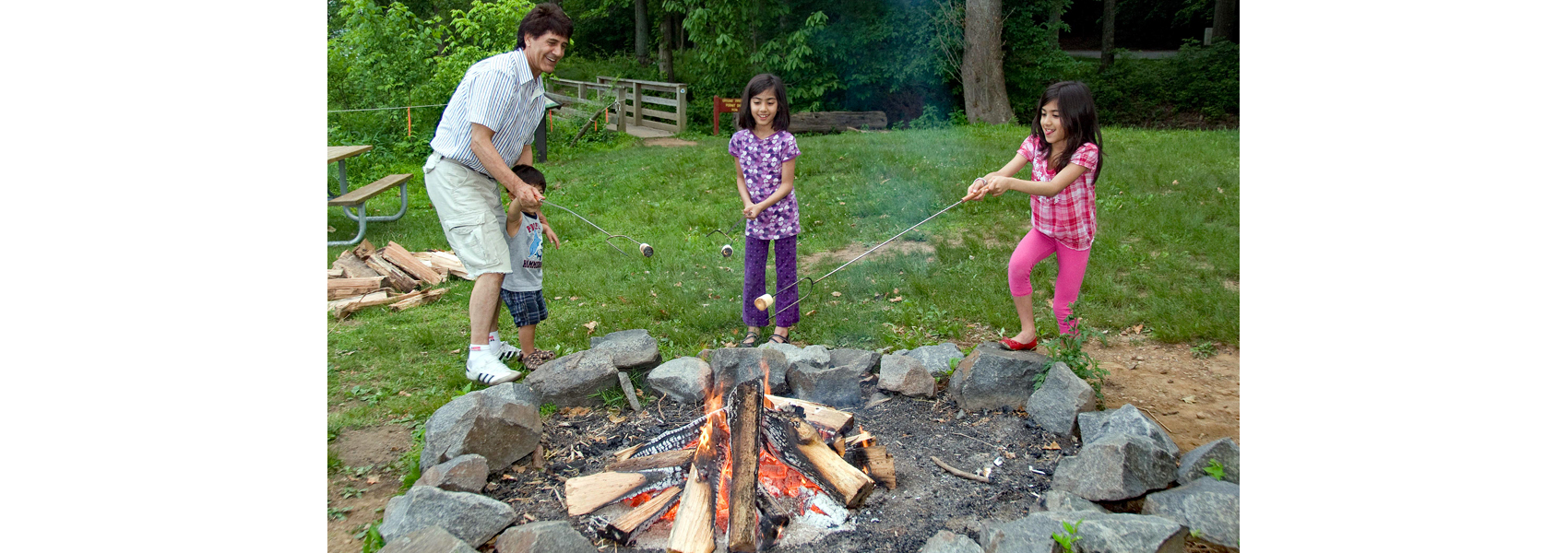 A family cooks a meal on sticks over a campfire