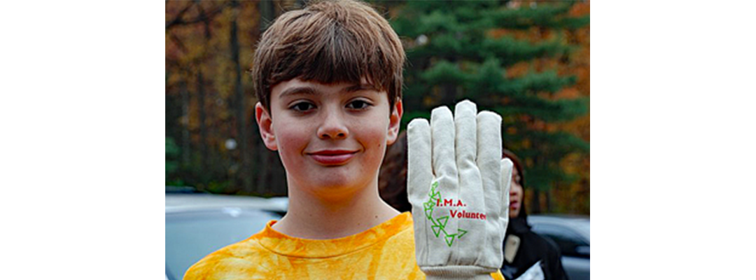 A young boy holds up his gloved hand with I.M.A. Volunteer stitched on it