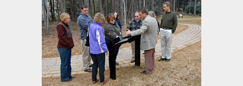 A guide talks to a group of visitors about an interpretive sign at Ox Hill.