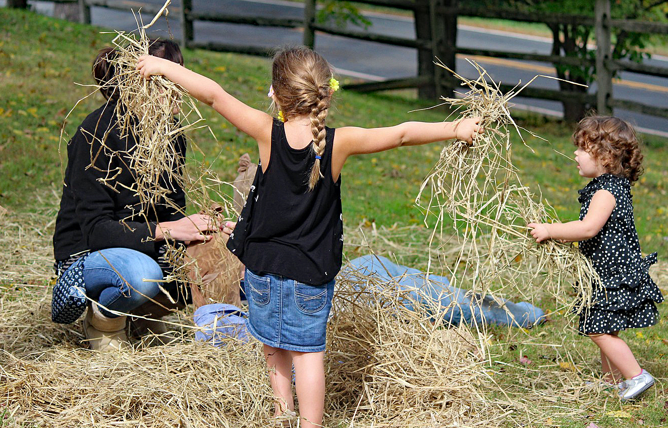 Young girls holds handfuls of straw to stuff in a scarecrow
