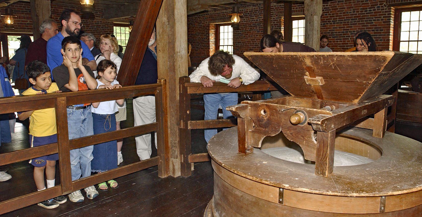 A group of people on a tour looks at a grinding stone in the mill