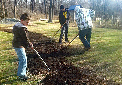 Three scouts rake mulch along a trail