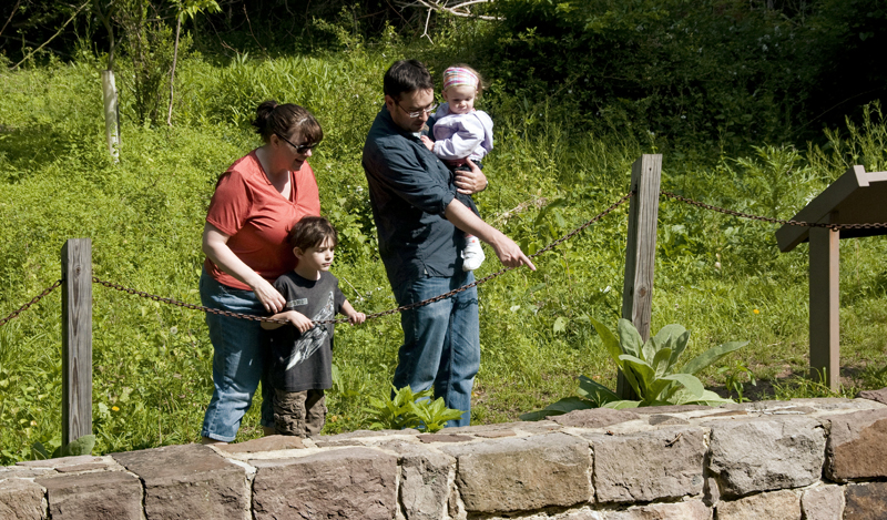 A father holding a child points at something inside the remnants of a historic house