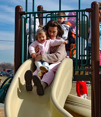 Young mother holds a child on her lap as they go down a slide