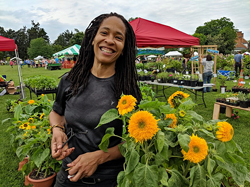 A smiling woman stands next to blooming flowers